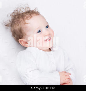 Adorable laughing little baby wearing a warm knitted jacket on a white blanket