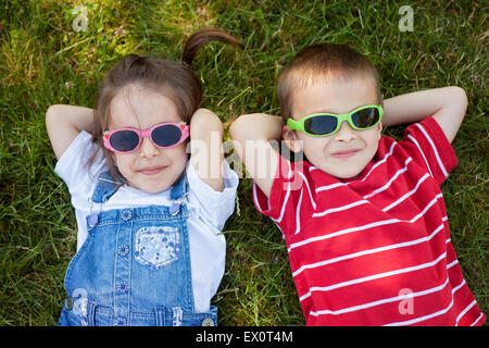 Sweel little boy and girl, wearing glasses, smiling, laying on the grass in the park Stock Photo