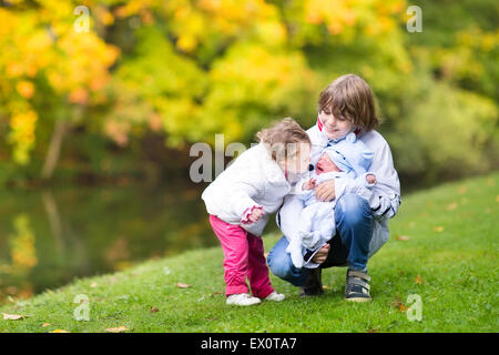 Brother and his little toddler sister comforting and kissing their newborn crying baby brother on a walk in a autumn park Stock Photo