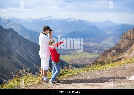 Young father and his teenager son taking pictures of a beautiful valley in the mountains Stock Photo