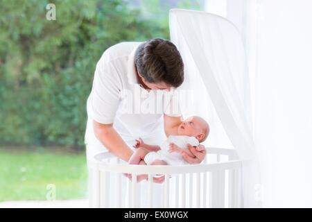 Happy young father putting his newborn baby in a white crib with canopy Stock Photo