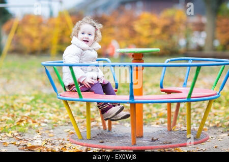 Cute smiling baby girl having fun at the playground in autumn Stock Photo