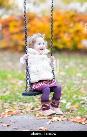 Happy laughing toddler girl playing on a swing with golden autumn trees in the background Stock Photo