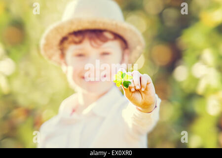 Lucky happy boy in hat holds four leaf clover Stock Photo