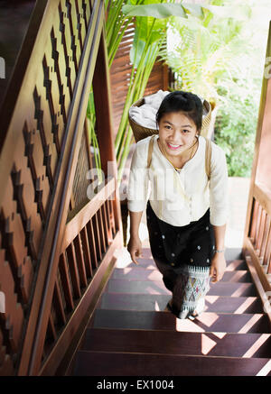 A chamber maid carries room towels in a basket on her back at 3 Nagas by Alila Hotel. Luang Prabang, Laos. Stock Photo