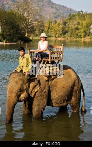 A Lao woman and mahout ride an elephant on the Khan River. Stock Photo