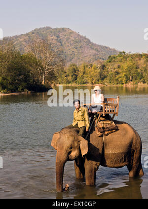 A Lao woman and mahout ride an elephant on the Khan River. Luang Prabang, Laos. Stock Photo