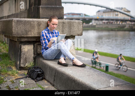 Teen girl sitting with the tablet outdoors in the city near the river. Stock Photo