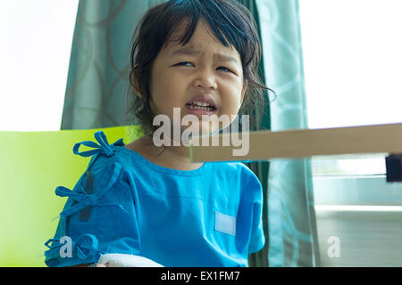 Illness asian kids crying, sit on a chair in hospital, saline intravenous (IV) on hand Stock Photo
