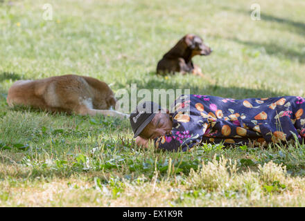 Sofia, Bulgaria - June 11, 2015: A homeless man is sleeping on a meadow in the center of Sofia with homeless dogs next to him. Stock Photo