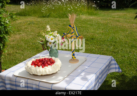 Table in a garden decorated with a newly made strawberry cake, midsummer pole and flowers Stock Photo