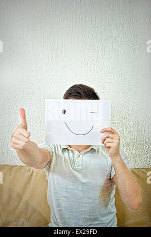 Unknown man winking and holding out a raised thumb up. Male model claims success in living room indoor. Stock Photo
