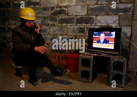 A labourer uses his mobile phone while watching a broadcast of China's Premier Wen Jiabao delivering his government work report Stock Photo