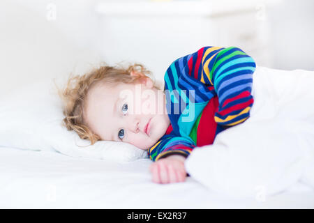 Cute toddler girl waking up in the morning in a sunny white bedroom Stock Photo