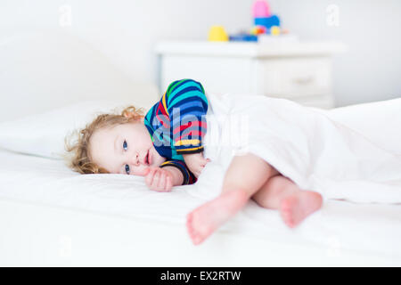 Adorable toddler girl waking up in the morning in a sunny white bedroom Stock Photo