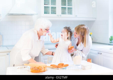 Funny toddler girl playing in a kitchen, having fun baking an apple pie with her grandmothers Stock Photo