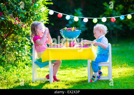 Children grilling meat. Family camping and enjoying BBQ. Brother and sister at barbecue preparing steaks and sausages. Stock Photo