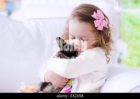 Child playing with a real rabbit. Kids play with pets. Little girl holding bunny. Children and animals at home or preschool. Stock Photo