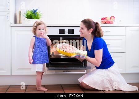 Mother and child bake a pie. Young woman and her daughter cook in a white kitchen. Kids baking pastry. Stock Photo