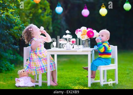 Garden birthday party for children. Kids outdoor celebration. Little boy and girl drinking tea and eating cake in the backyard Stock Photo