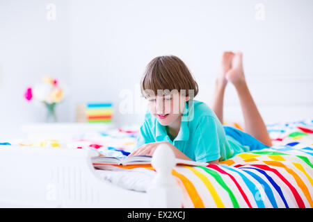 School age boy reading a book in bed. Children read books. Kids learning. Student kid doing homework in a sunny bedroom. Stock Photo