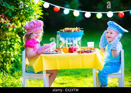 Children grilling meat. Family camping and enjoying BBQ. Brother and sister at barbecue preparing steaks and sausages. Stock Photo