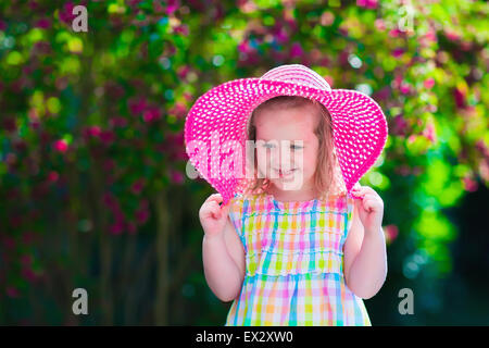 Little cute girl with flowers. Child wearing a pink hat playing in a blooming summer garden. Kids gardening. Children play outdo Stock Photo