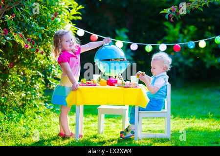 Children grilling meat. Family camping and enjoying BBQ. Brother and sister at barbecue preparing steaks and sausages. Stock Photo