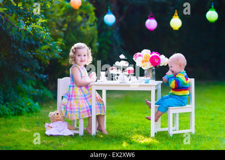 Garden birthday party for children. Kids outdoor celebration. Little boy and girl drinking tea and eating cake in the backyard Stock Photo