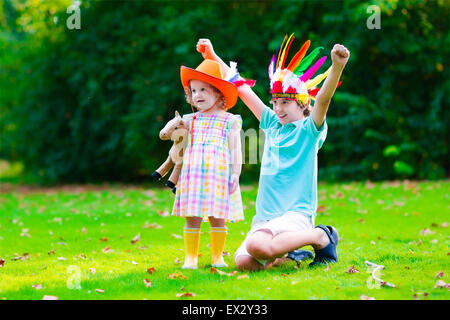 Kids in cowboy and cowgirl costumes playing outdoors. Children play with toy horse. Boy in Native American hat on Thanksgiving Stock Photo