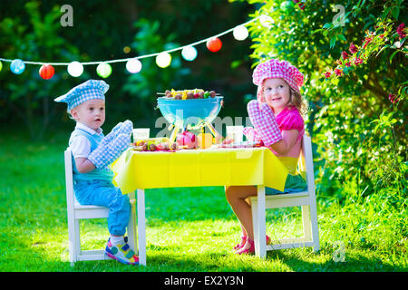 Children grilling meat. Family camping and enjoying BBQ. Brother and sister at barbecue preparing steaks and sausages. Stock Photo