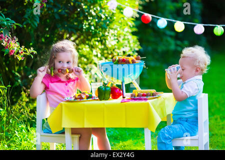 Children grilling meat. Family camping and enjoying BBQ. Brother and sister at barbecue preparing steaks and sausages. Stock Photo