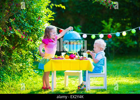 Children grilling meat. Family camping and enjoying BBQ. Brother and sister at barbecue preparing steaks and sausages. Stock Photo