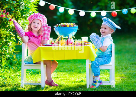 Children grilling meat. Family camping and enjoying BBQ. Brother and sister at barbecue preparing steaks and sausages. Stock Photo