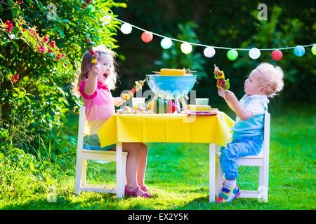 Children grilling meat. Family camping and enjoying BBQ. Brother and sister at barbecue preparing steaks and sausages. Stock Photo