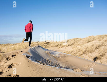 Mature man running on sand dunes covered in frost at Seaton Carew on the north east coast of England. UK Stock Photo