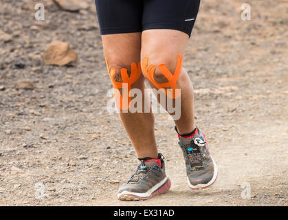 Heavy female runner wearing elastic therapeutic tape (KT Tape, Kinesiology tape..) on knees during trail race Stock Photo