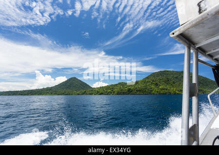 A speed motor boat creates wake with a volcano in the background in Kimbe Bay, Papua New Guinea. Stock Photo