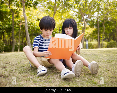 asian boy and girl reading in a park. Stock Photo