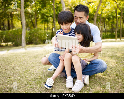 asian father and children using tablet in park Stock Photo