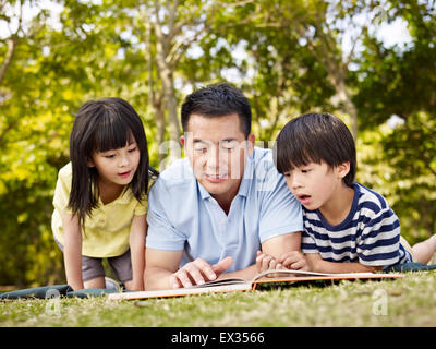 father and children reading a book outdoors. Stock Photo