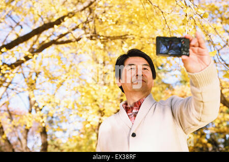 Senior Japanese man taking a selfie in a city park in Autumn
