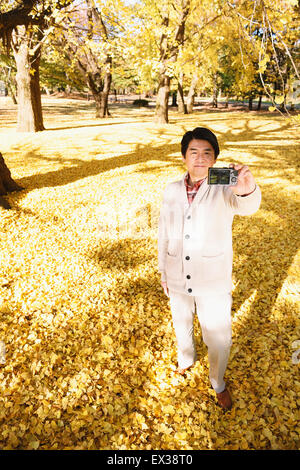 Senior Japanese man taking a selfie in a city park in Autumn