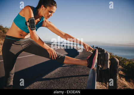 Female runner stretching her legs outdoor before running. Woman doing leg stretch exercises on road guardrail. Stock Photo