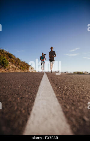 Low angle shot of two young people running on the road. Jogging on country road on a summer day. Stock Photo