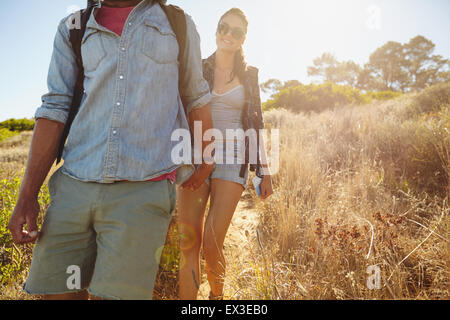 Image of young woman hiking in mountains with her boyfriend in front. Couple walking downhill on summer vacation. Stock Photo