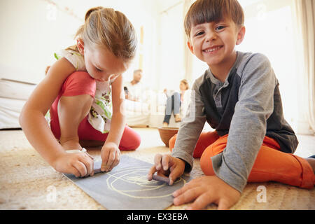 Indoor shot of happy little children drawing and coloring sitting on floor with parents in background at home Stock Photo