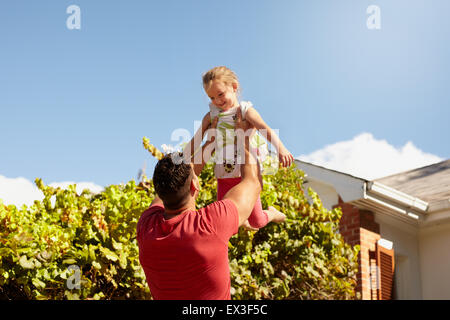 Young man lifting his daughter high in the air. Happy father and daughter playing in their backyard on a sunny day. Stock Photo