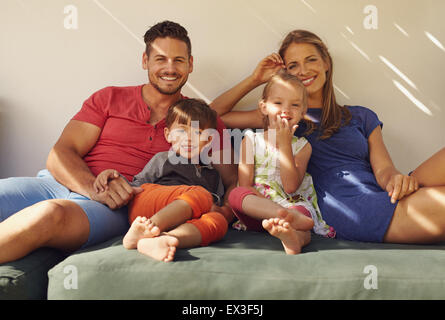 Parents sitting outside with children on couch in backyard. Happy young family relaxing on patio, looking at camera smiling. Stock Photo