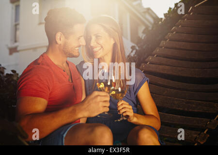Happy young couple sitting on hammock toasting wine and looking at each other smiling. Loving young couple relaxing with a glass Stock Photo